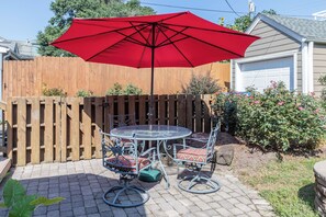 Eine Terrasse mit einem runden Tisch, zwei Stühlen, einem roten Sonnenschirm und einem Holzzaun.