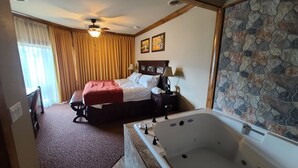 A hotel room with a bed, a bathroom with a bathtub, a ceiling fan, and a stone wall. - Gatlinburg Resort Getaway (Gatlinburg)