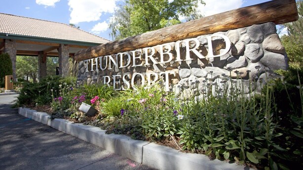 A sign for Thunderbird Resort with a stone and wooden structure, surrounded by a landscaped garden with various plants and flowers.