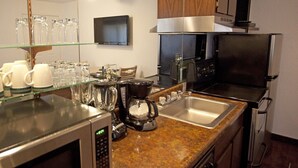 A modern kitchen with stainless steel appliances, a coffee maker, and a glass display of mugs.