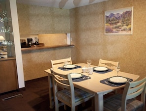 A dining area with a table set for four, chairs, a coffee machine, and a painting on the wall.