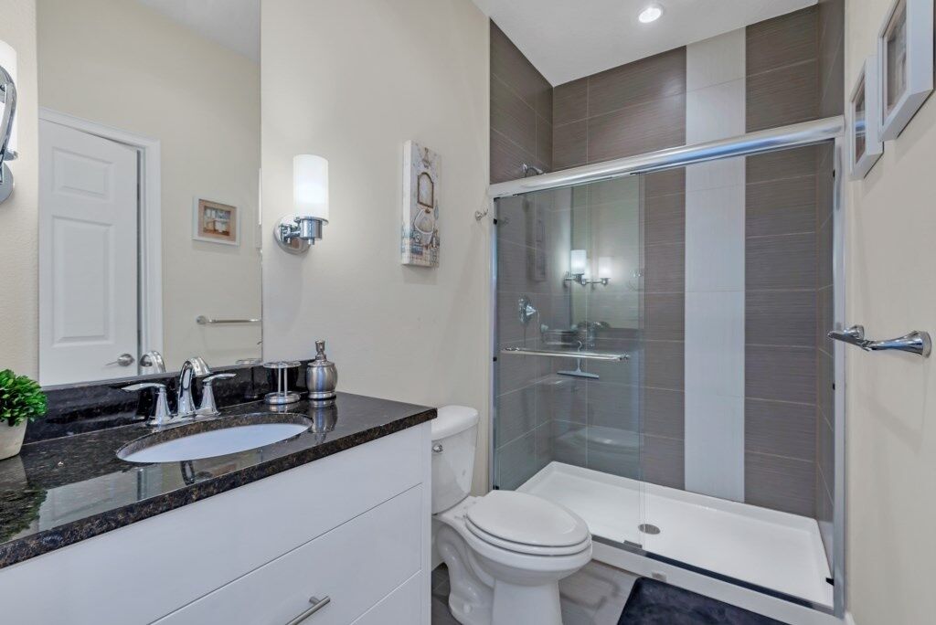 A modern bathroom with a glass-enclosed shower, a white toilet, and a granite countertop with a sink.