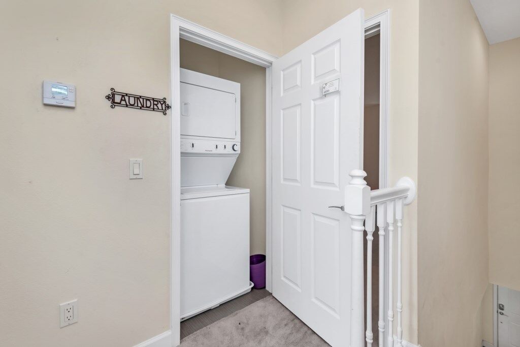 A laundry room with a white washer and dryer, a purple trash bin, and a sign that reads "Laundry".