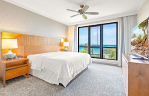 Une chambre d’hôtel avec un grand lit, un ventilateur de plafond, une table de chevet avec une lampe, une télévision et une vue sur l’océan.