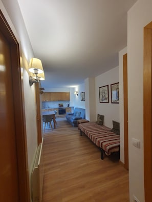 A hallway leading to a living area with a sofa, a bed, and a dining table.