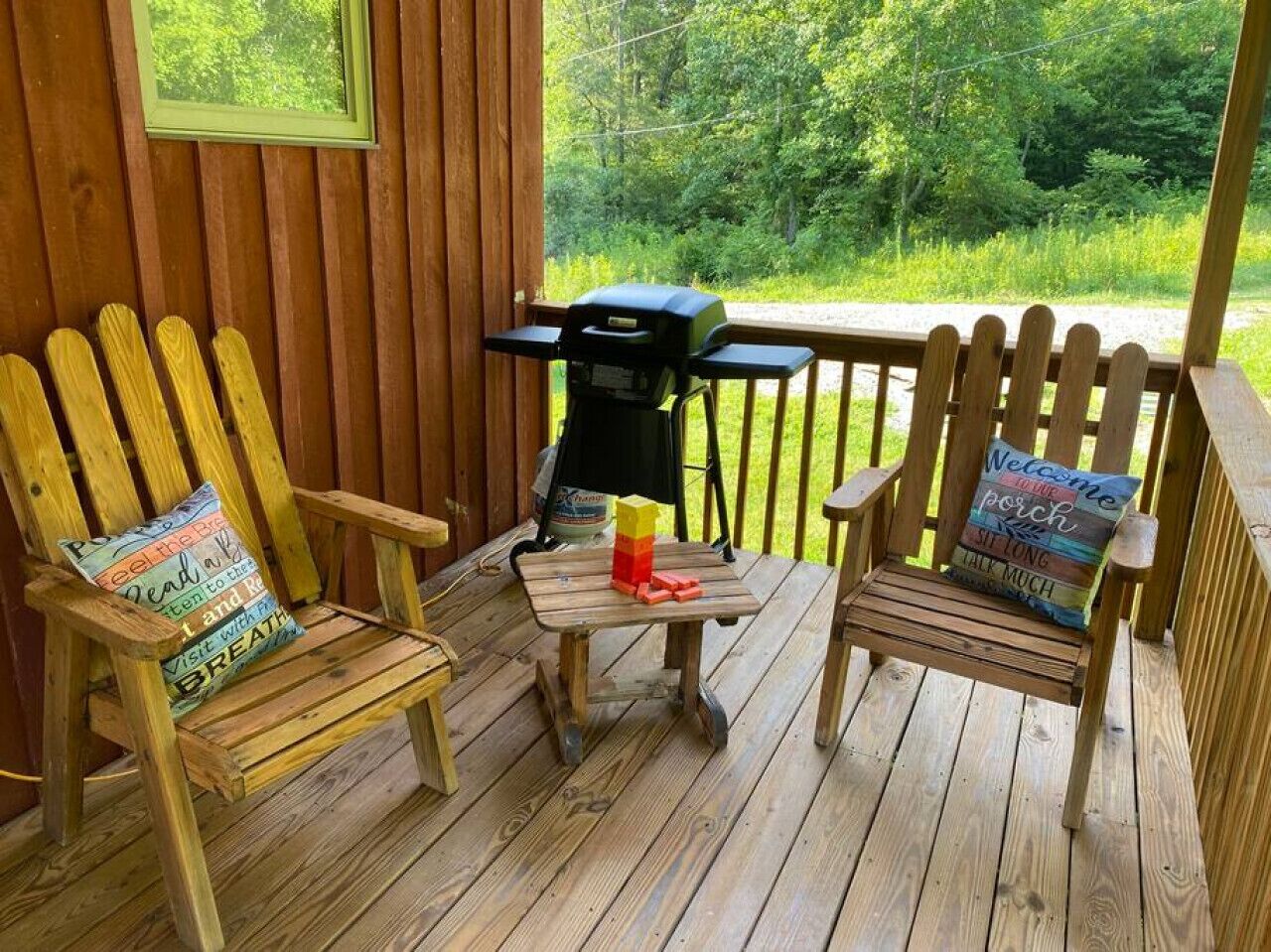 A wooden deck with two Adirondack chairs and a grill.