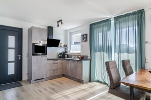 Una cocina moderna con horno empotrado, microondas y cafetera. Cuenta con un comedor con mesa de madera y dos sillas.