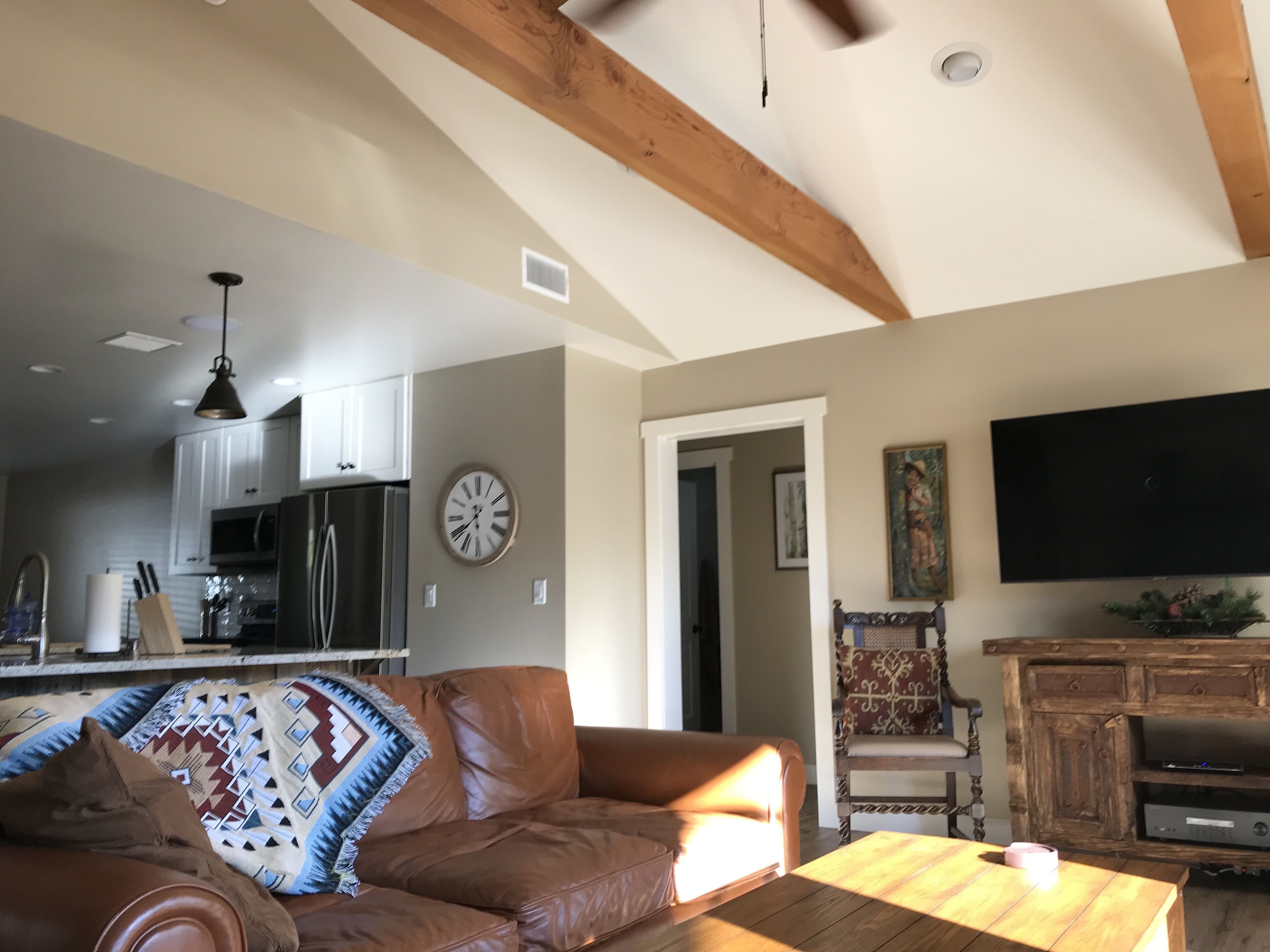 Un salon spacieux avec un canapé en cuir, une table basse en bois et un téléviseur fixé au mur.