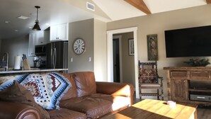 A spacious living room with a leather sofa, a wooden coffee table, and a TV mounted on the wall.