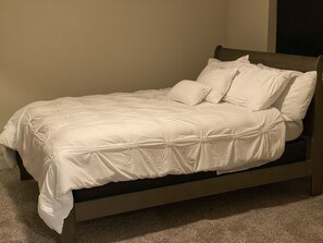 Cozy bed with a white bedspread and pillows, set against a plain wall.