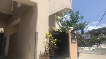 Un edificio con facciata color beige, un cancello nero e un cartello con caratteri giapponesi. Davanti al cancello ci sono piante in vaso.