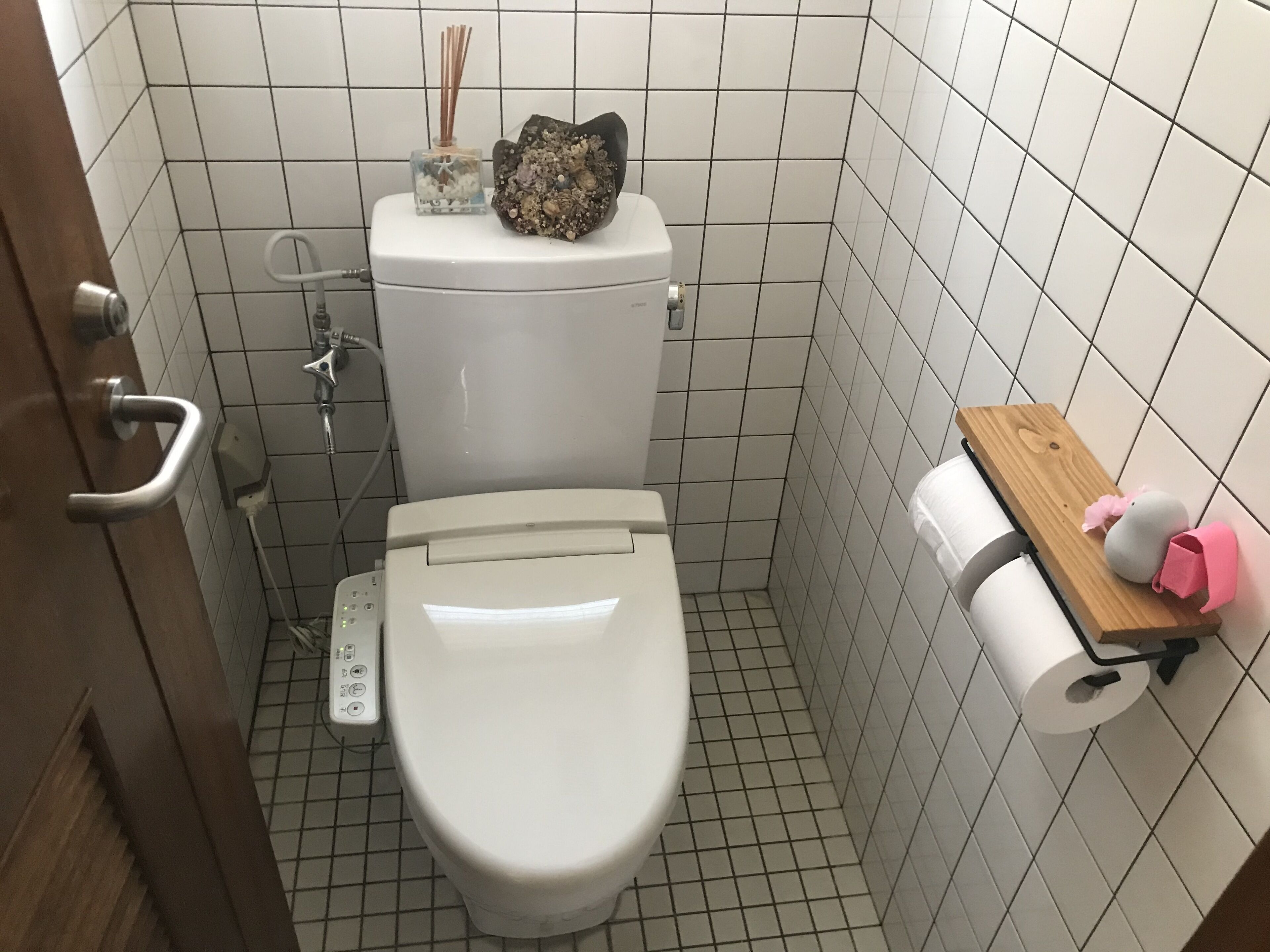 Un baño pequeño con azulejos, un inodoro, un dispensador de desinfectante para manos y un porta papel higiénico.