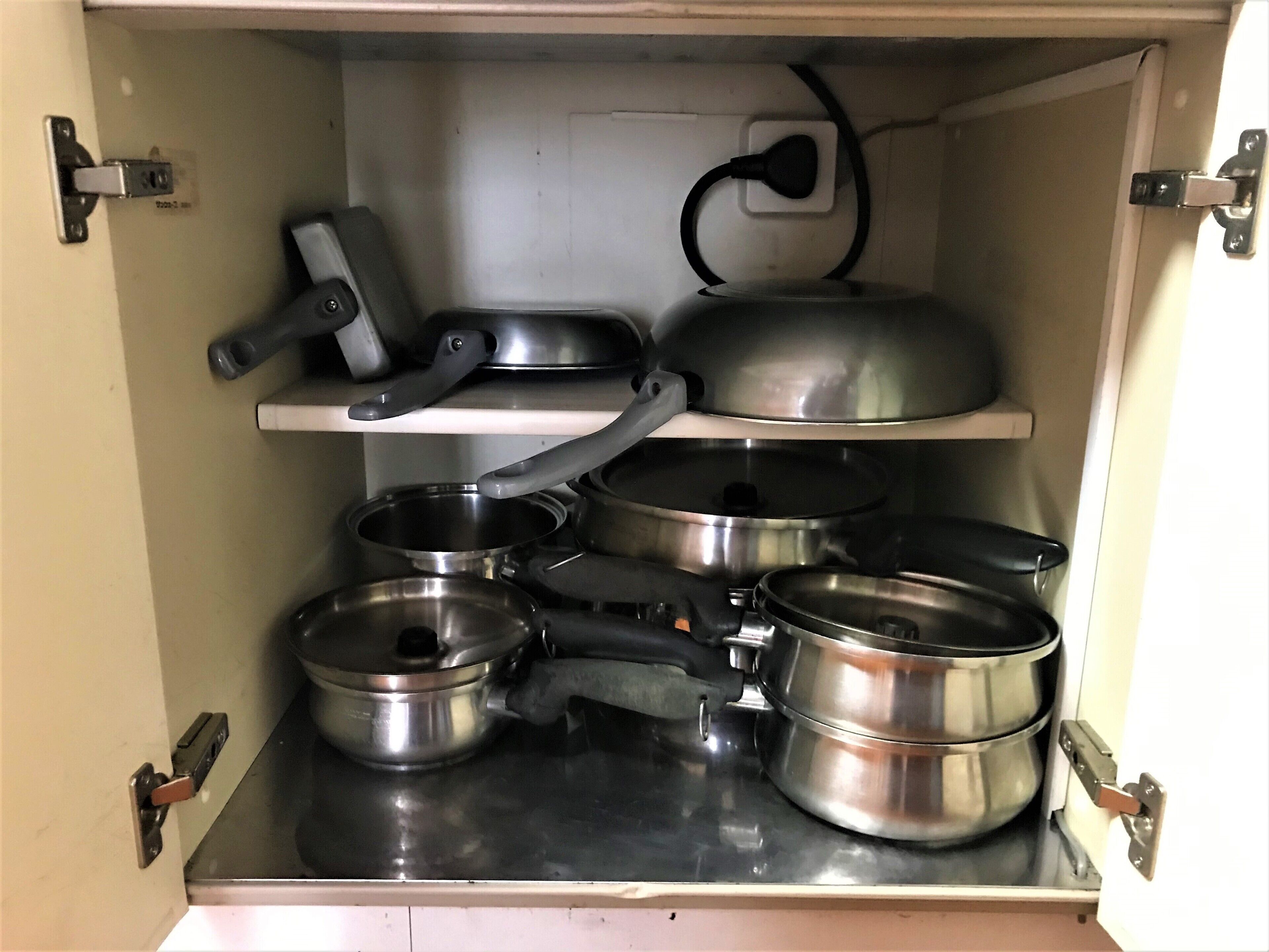 Ein Küchenschrank mit Edelstahlkochgeschirr, darunter Töpfe und Pfannen, sowie einem eingebauten Herd.