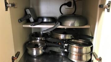 Ein Küchenschrank mit Edelstahlkochgeschirr, darunter Töpfe und Pfannen, sowie einem eingebauten Herd.