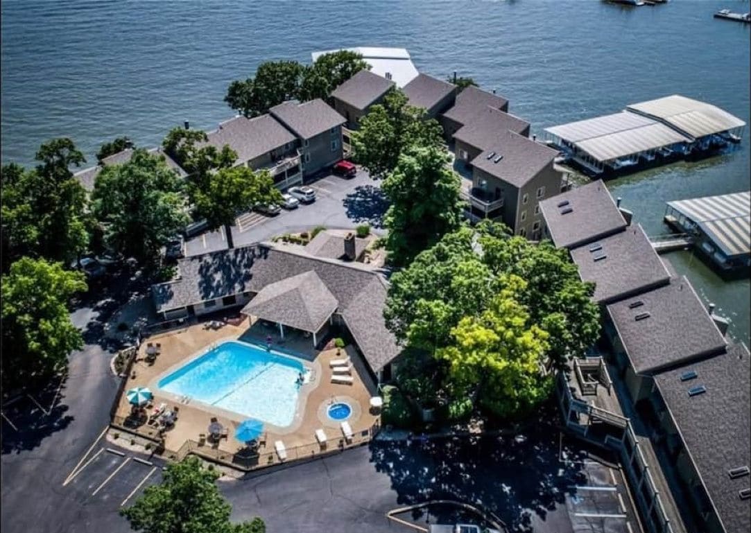 Vista aérea de un resort con piscina, varias construcciones y barcos en el agua.