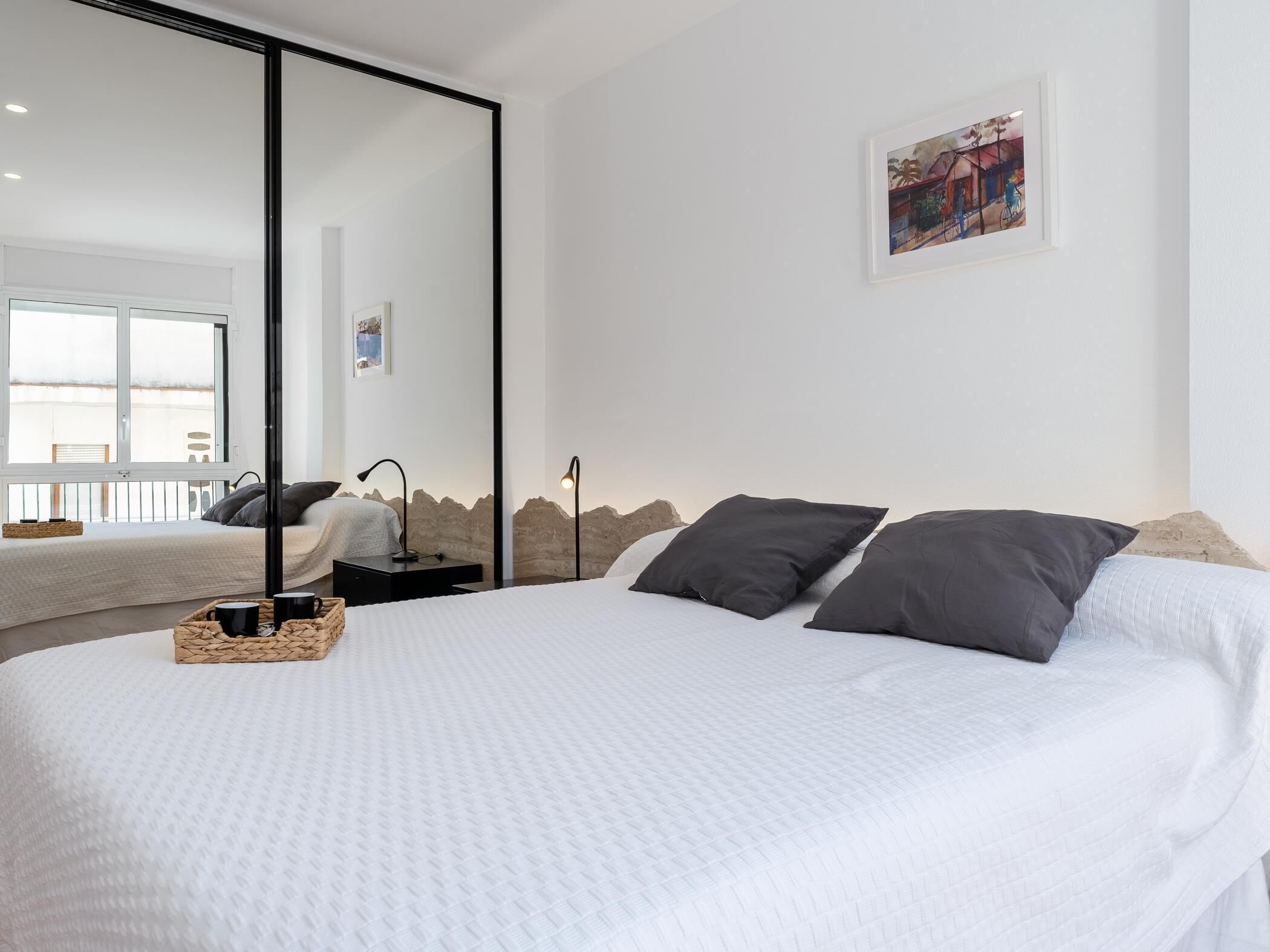 A modern bedroom with a large bed, a bedside table, a lamp, and a framed picture on the wall.