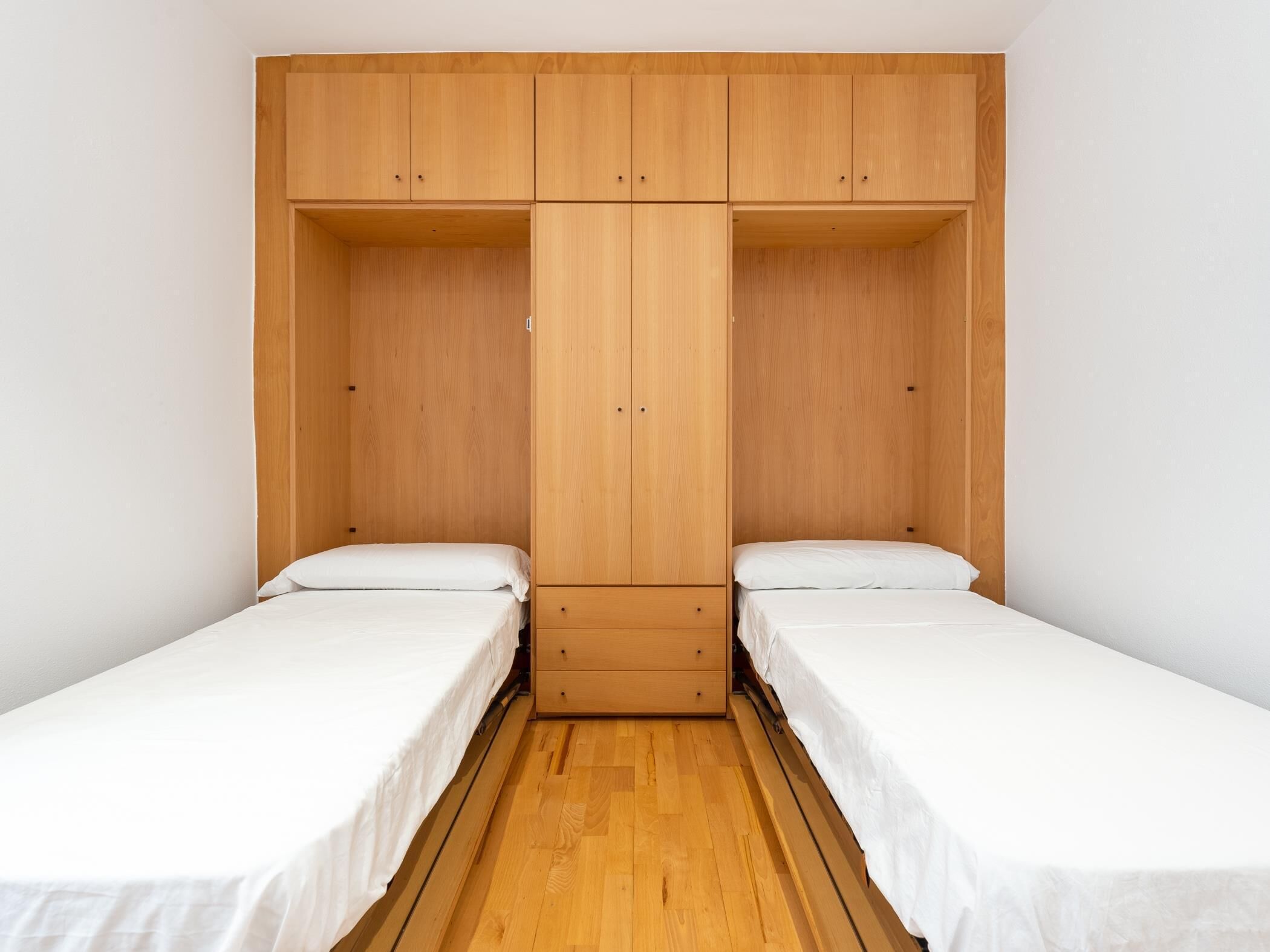 A room with two single beds, wooden wardrobe, and a wooden floor.