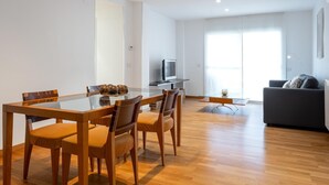 A modern living room with a glass dining table, wooden chairs, a grey sofa, and a television. - Spacious apartment with A/C and heating (L'Ametlla de Mar)