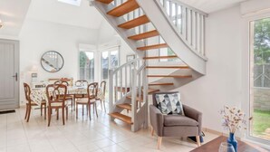A spacious living area with a modern staircase, a dining table with chairs, and a cozy seating area with a vase of flowers. - Armorique by Interhome (Carnac)