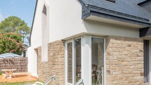 A modern house with a stone exterior, a glass door leading to a patio area with two lounge chairs and a table. - Armorique by Interhome (Carnac)