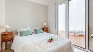 A modern bedroom with a large bed, two bedside tables with lamps, and a sliding glass door leading to a balcony. - Armorique by Interhome (Carnac)