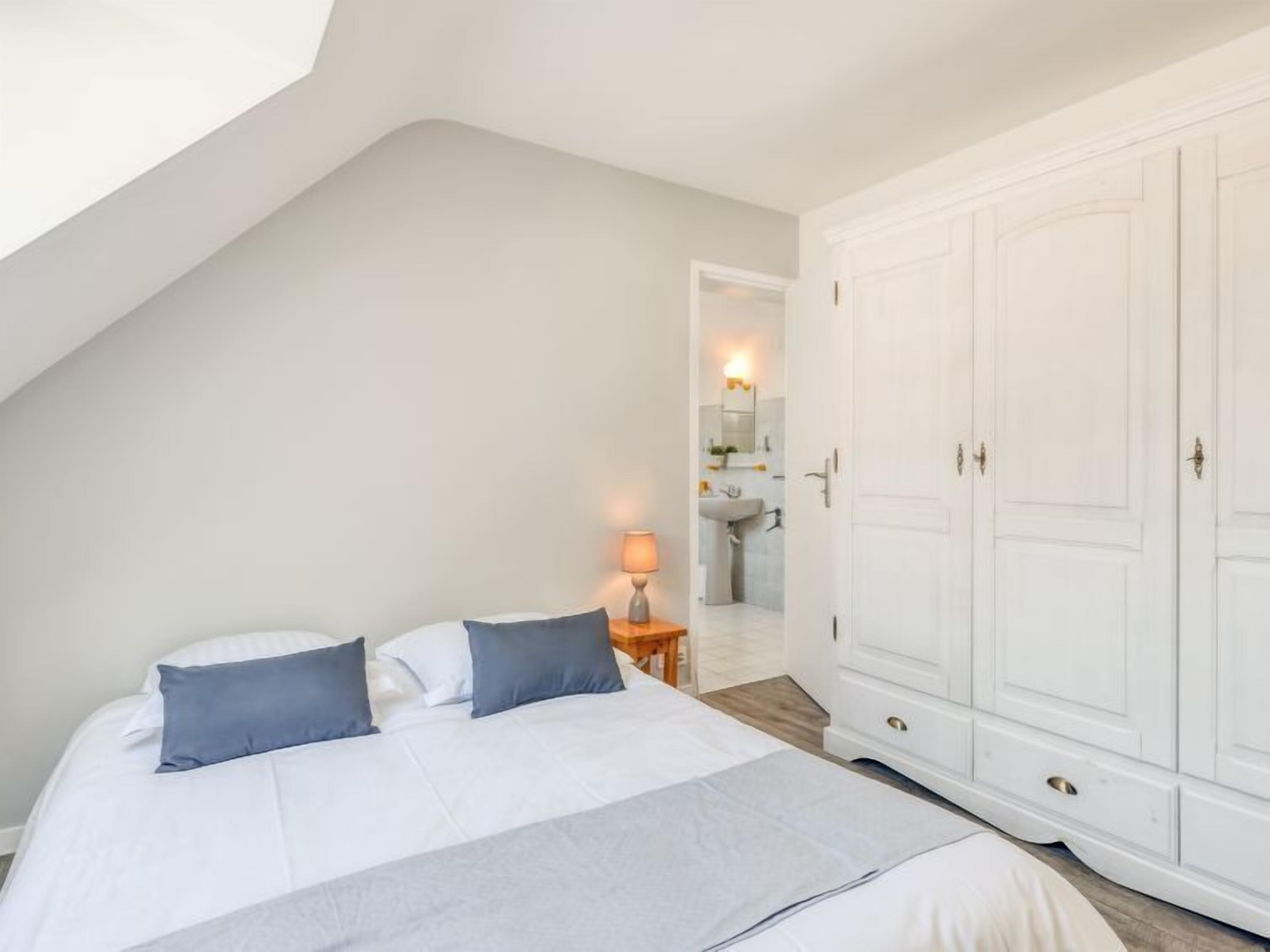 Ein Schlafzimmer mit Bett, Nachttisch, Kleiderschrank und einem durchgehenden Türrahmen einsehbarer Badezimmer.