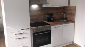 A modern kitchen with white cabinets, a black stove, a coffee maker, and a sink. - Lower vacation apartment between Tauber Valley, Odenwald and Bauland (Ahorn)