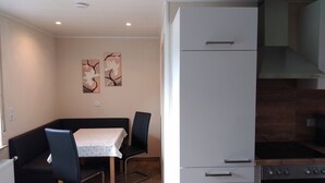 A compact kitchen with a built-in oven, a refrigerator, and a dining area with a table and chairs. - Lower vacation apartment between Tauber Valley, Odenwald and Bauland (Ahorn)