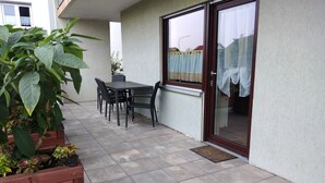 A patio with a table and chairs, a wooden planter with plants, and a sliding glass door. - Lower vacation apartment between Tauber Valley, Odenwald and Bauland (Ahorn)