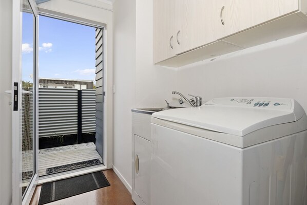 A compact laundry room with a washing machine, a sink, and a sliding glass door leading to a balcony.