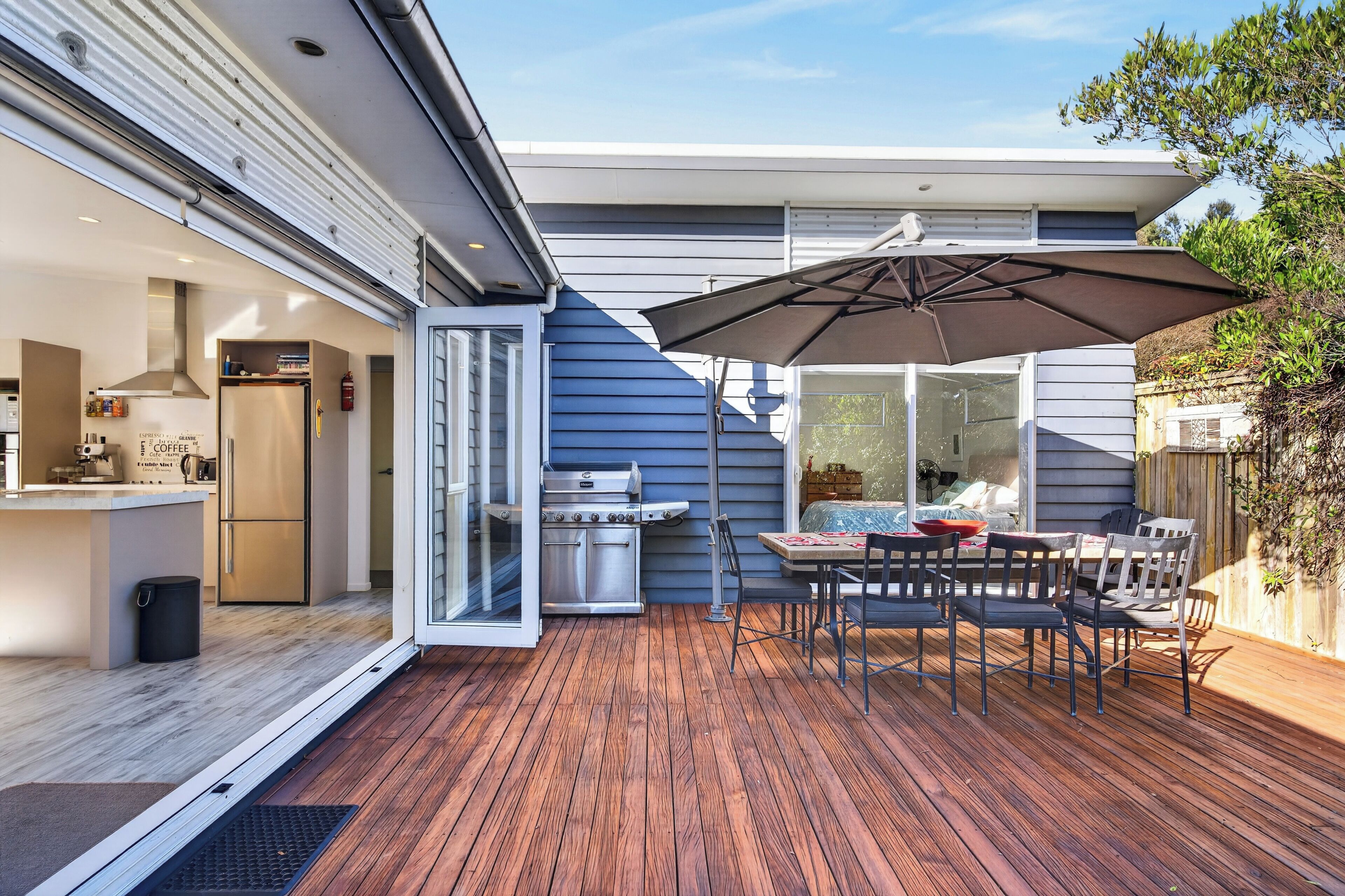 A modern outdoor patio with a wooden deck, a grill, and a dining table with chairs.