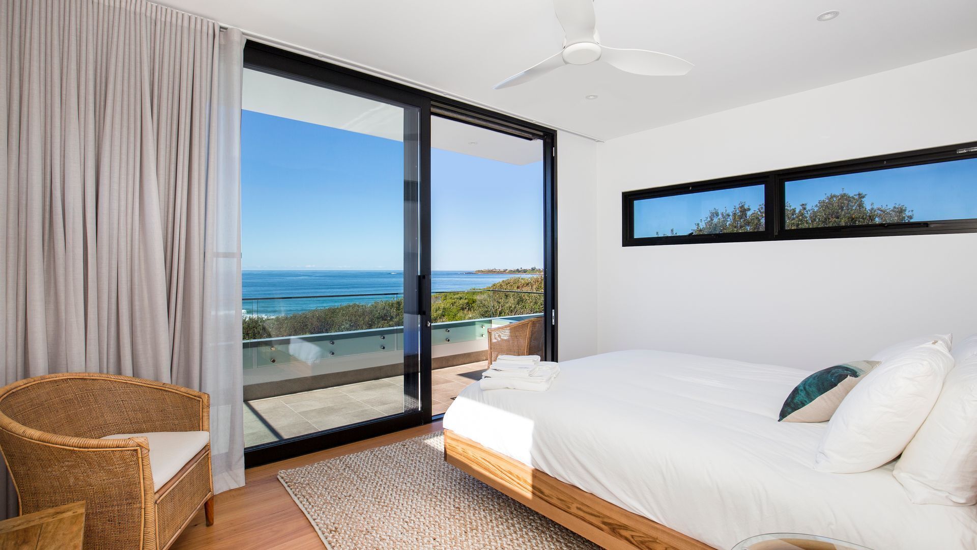 A bedroom with a large sliding glass door leading to a balcony with a view of the ocean.