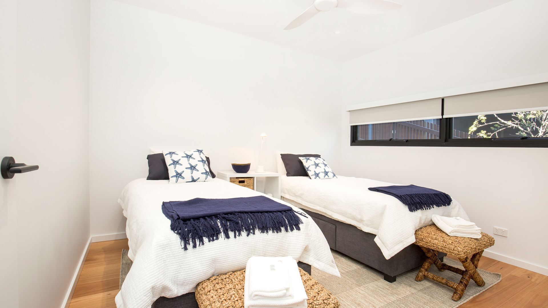 A modern bedroom with two beds, a small table, a bench, and a window with a view.