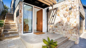 Ein modernes Haus mit Steinaußenwand, einer Holztreppe und einer Glastür, die zu einem Holzinnenraum führt.