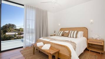 A bedroom with a large bed, a wooden nightstand, a small table with towels, and a view of the outdoors.