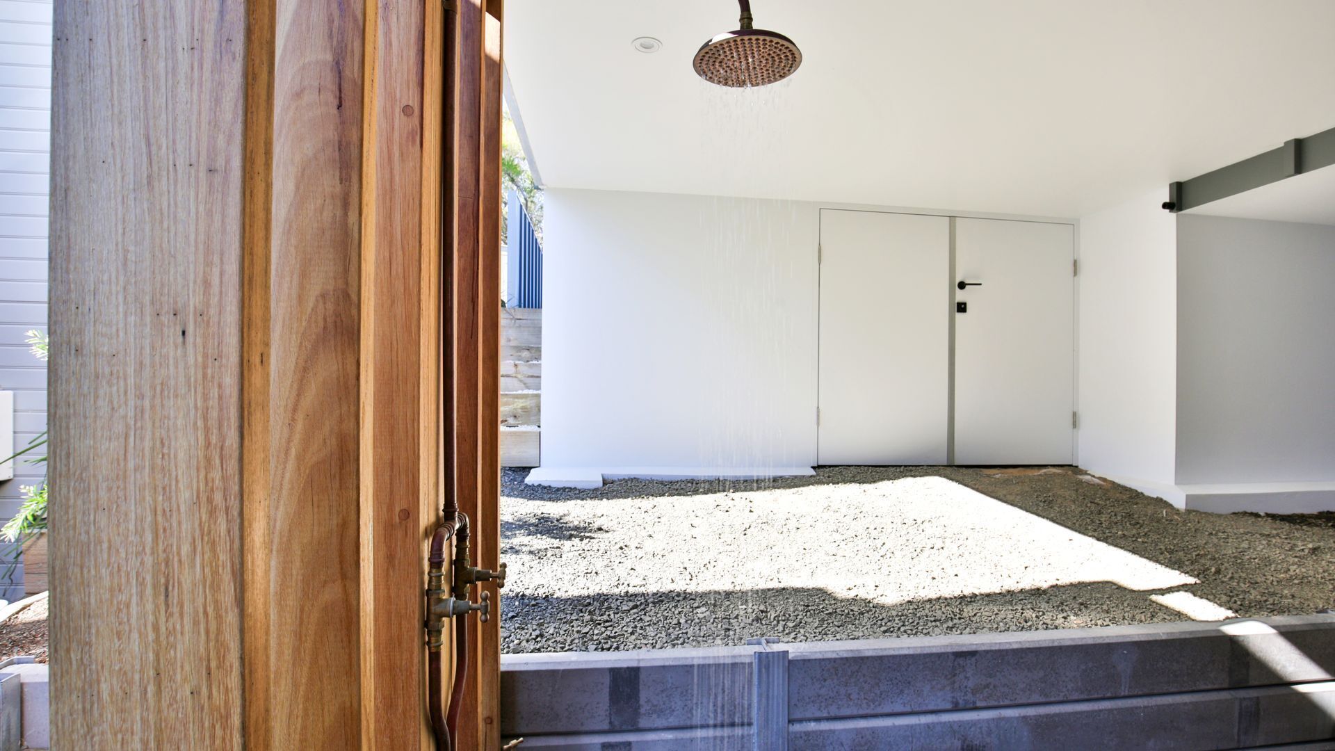 Quarto com porta branca, área de chuveiro com chuveiro e piso de brita.