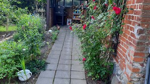 Un chemin de jardin mène à un bâtiment en briques doté d’une porte en verre.