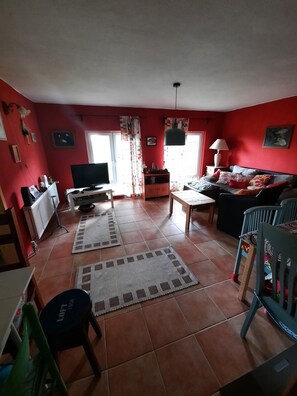 A living room with a red wall, a television, a sofa, a coffee table, and a lamp.