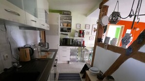 Une cuisine étroite avec des meubles blancs, un plan de travail noir et un tapis à rayures. On y trouve une étagère en bois ornée de poteries et un luminaire suspendu.