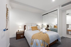 A modern bedroom with a large bed, bedside tables, a mirror, and a wall-mounted artwork.