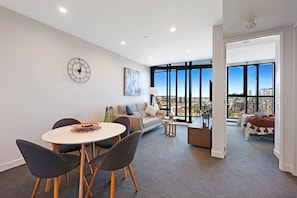Uma sala de estar moderna com área de jantar, um sofá, uma mesa de centro e uma grande janela com vista para a cidade.
