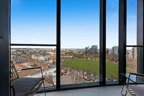 Quarto com grandes janelas que oferecem vista para a cidade, incluindo um campo esportivo.