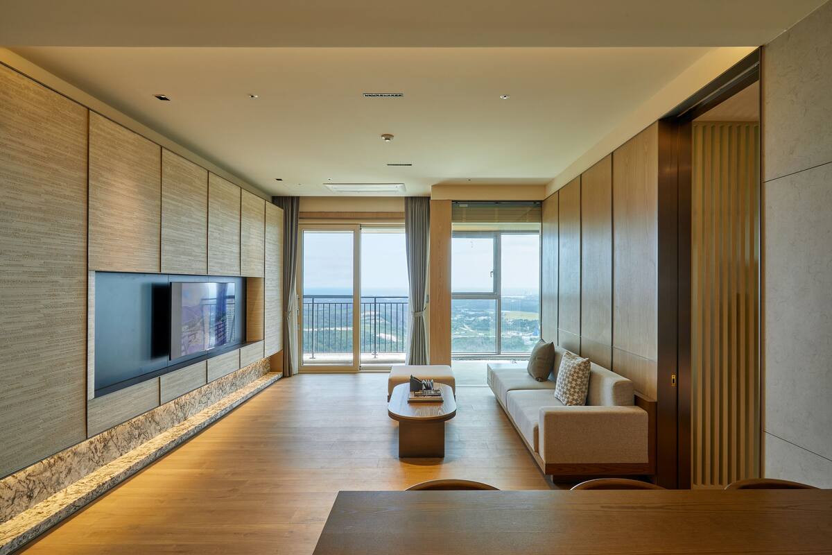 A modern living room with a flat-screen TV mounted on the wall, a sofa, a coffee table, and a dining table.