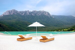 A pool area with lounge chairs and an umbrella, overlooking a turquoise pool and a mountainous landscape. - Sono Felice Delpino (Goseong)