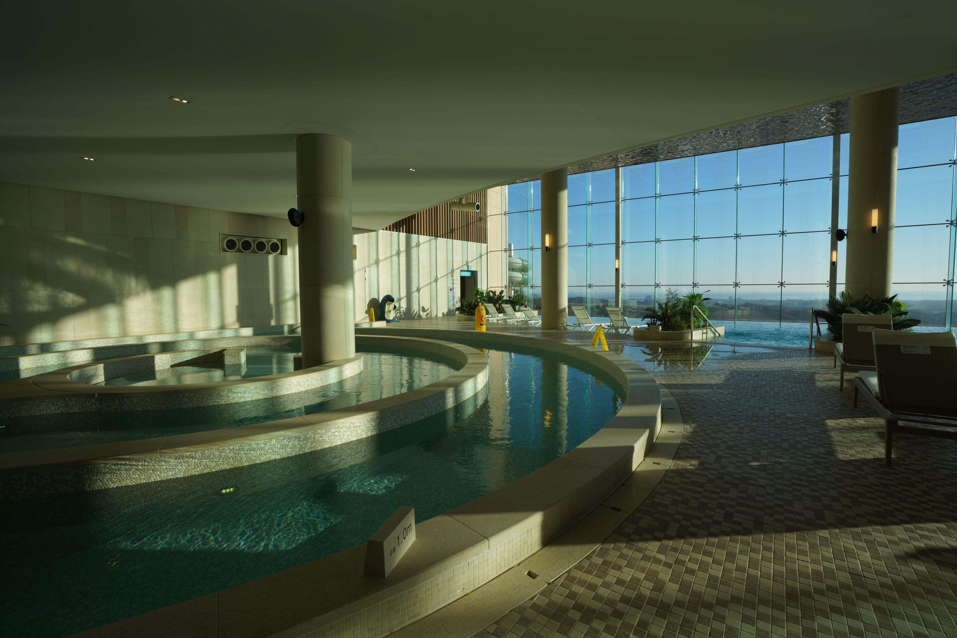 Una amplia piscina interior con vistas a la ciudad a través de grandes ventanales.