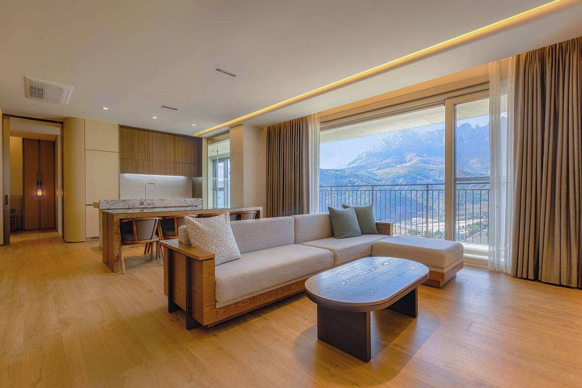 A modern living room with a sofa, coffee table, and a view of mountains through large windows.