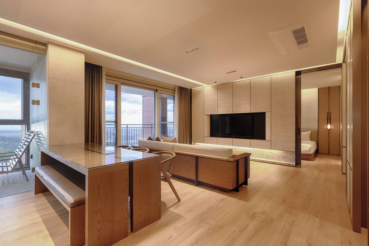 A modern living room with a wooden floor, a sofa, a TV, and a balcony with a view.