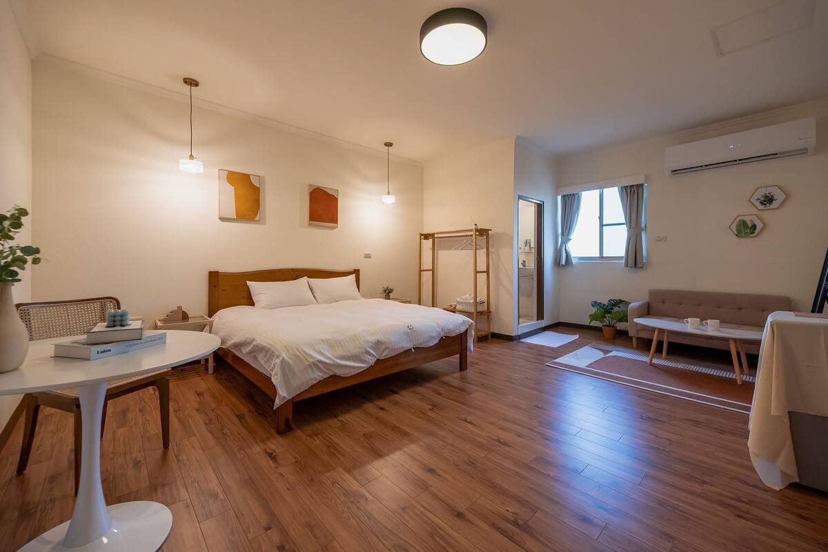 A modern bedroom with a wooden bed, bedside tables, a small table with a vase, and a sofa.