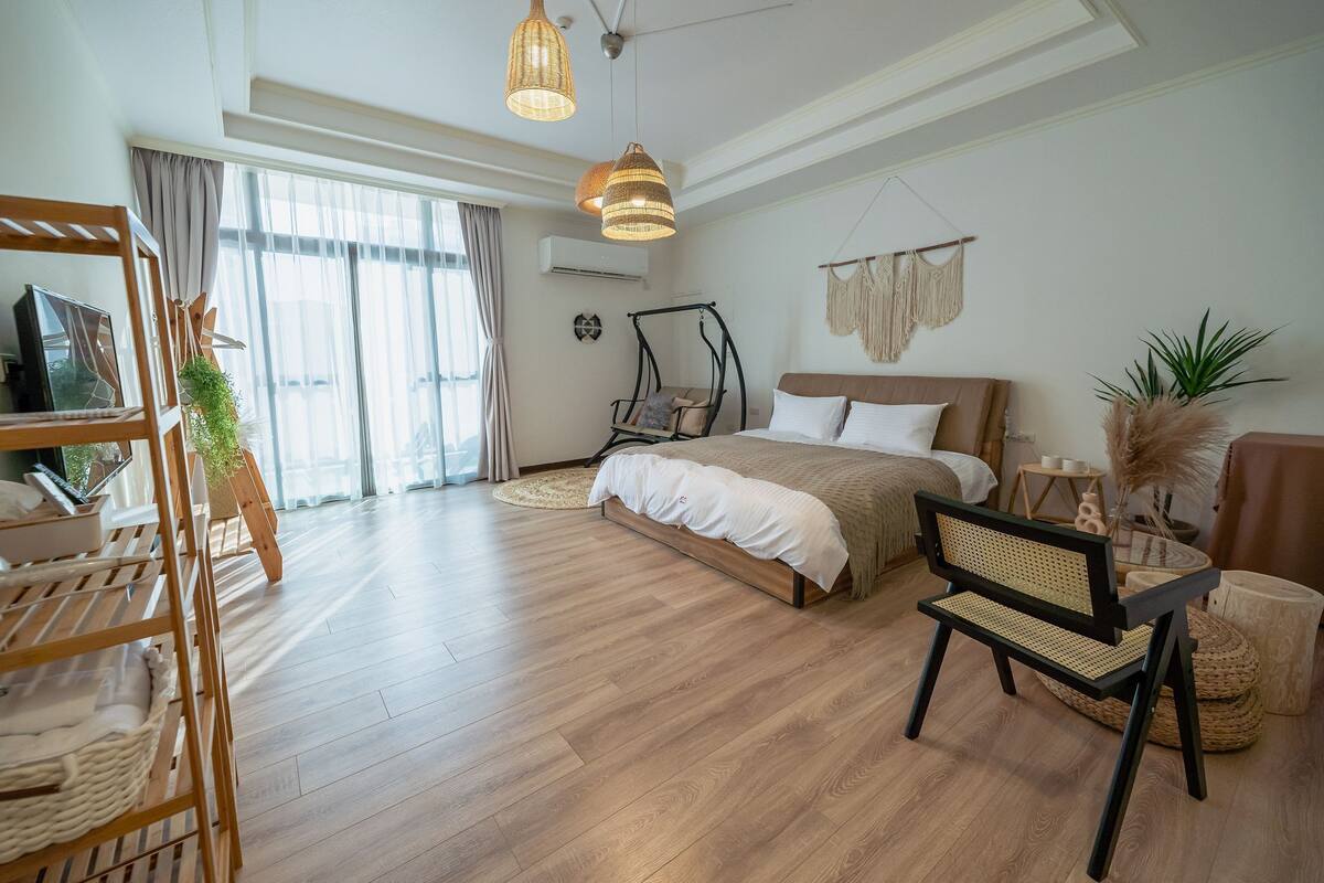 A spacious bedroom with a large bed, a wooden chair, a hanging chair, and a small table.