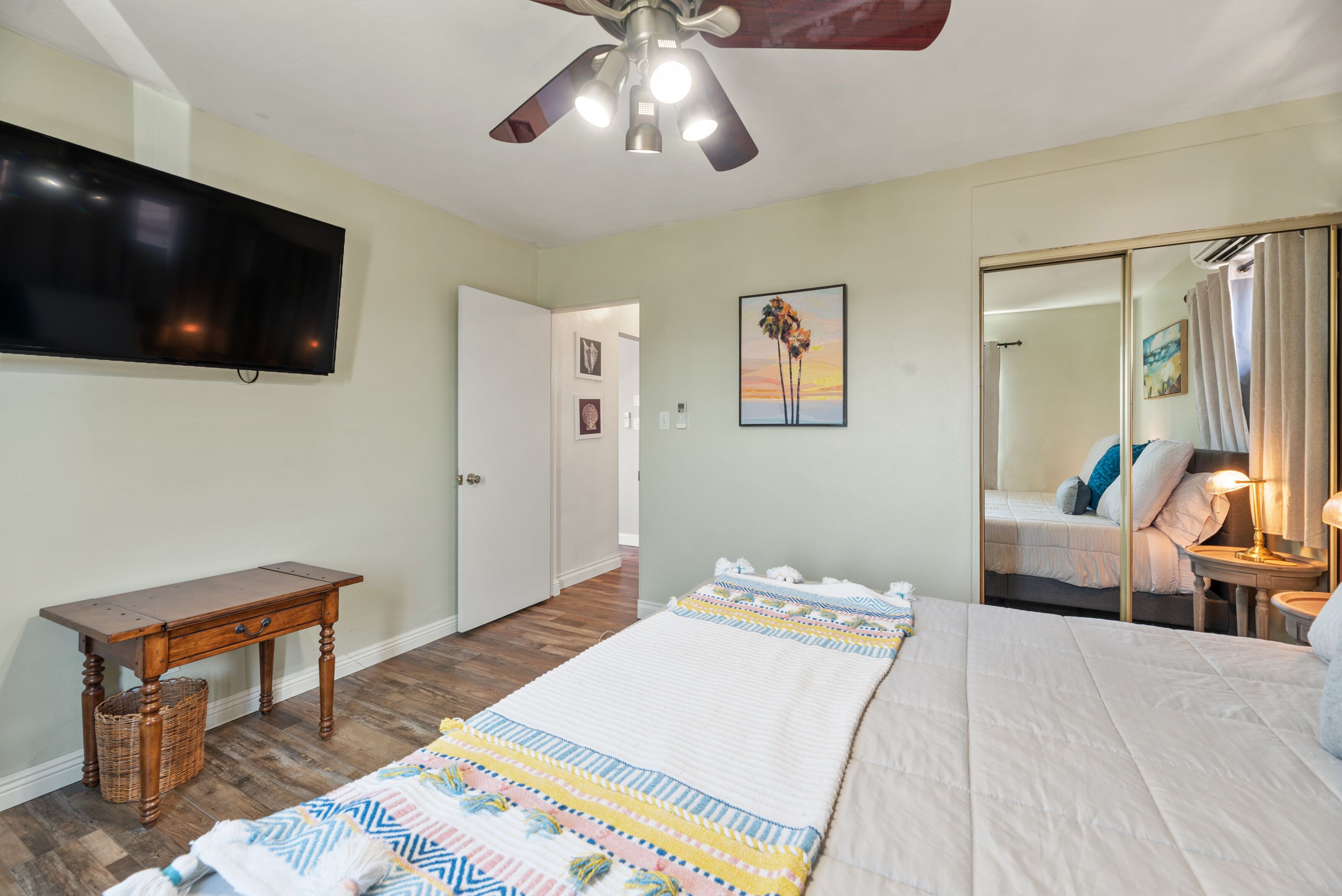 Un dormitorio con una cama, televisión, ventilador de techo, mesita de noche y una cesta de mimbre.
